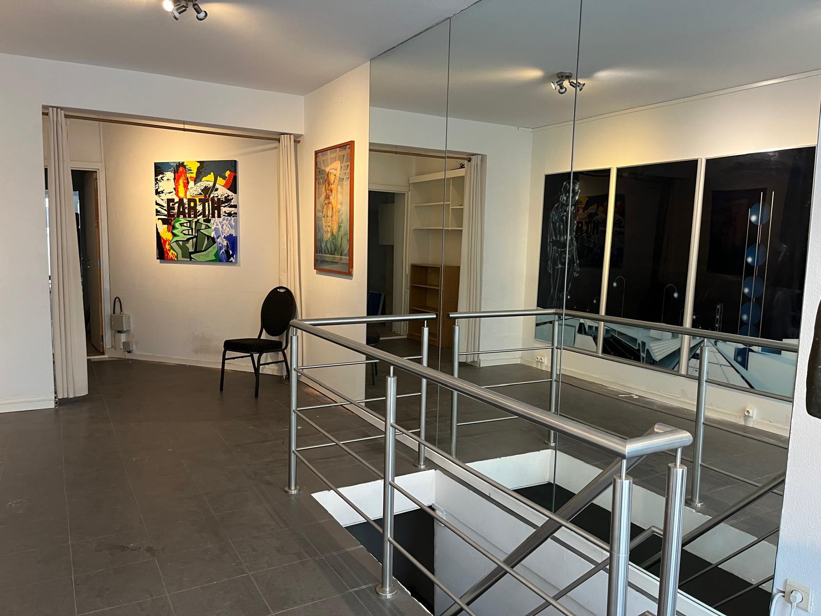 Overzicht van de tentoonstellingsruimte met schilderijen, spiegels en een trap